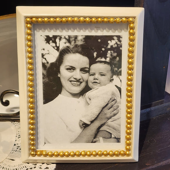 This white frame has a gorgeous gold bead trip surrounding the photo area.  It's a stylish way to display your favorite photo! It is backed in black velvet with an easel prop. It will stand for tabletop display. Stands/hangs horizontally or vertically.  Dust with a dry, soft cloth. Resin Frame measurement: 6 1/4