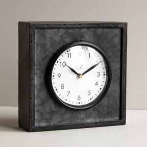 We love this clean contemporary/modern farmhouse-style tabletop clock! The black galvanized metal structure features a glass cover over the clock face sealed with a black rim. The bold black and white color allow this clock to be styled with ease within your bookcase or on your tabletop, while still maintaining a timeless feel.   Ticking mechanism requires an AA battery not included.  7.75 x 3 x 7.75"H; Clock face diameter: 4.5  Metal & Plexiglass