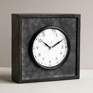 We love this clean contemporary/modern farmhouse-style tabletop clock! The black galvanized metal structure features a glass cover over the clock face sealed with a black rim. The bold black and white color allow this clock to be styled with ease within your bookcase or on your tabletop, while still maintaining a timeless feel.   Ticking mechanism requires an AA battery not included.  7.75 x 3 x 7.75