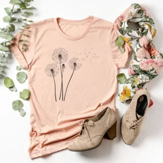 Our Dandelion t-shirt is the prettiest shade of peach, with four black dandelions on the front. These are so soft & comfy. You will love wearing them to ball games, bonfires, or running errands. The styling possibilities are endless. Roll up the sleeves, tie a side knot, front tuck, or wear it while lounging around the house. We guarantee that you will love the fit and the softness of this shirt.