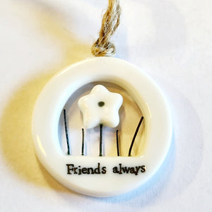 This little circular porcelain gift tag is sure to bring a little happiness to you or someone you give it to!  Inside the cut-out is a flower with stems around it; below it is the word "Friends Always." A jute rope is attached at the top for hanging.  1 1/4" Dia