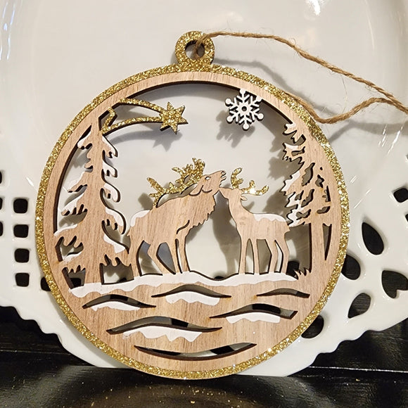 These two bucks are in a snowy forest with a snowflake on the top right and a shooting star on the top left. Gold glitter accents this natural wood ornament with white accents of snow on the ground and trees.
