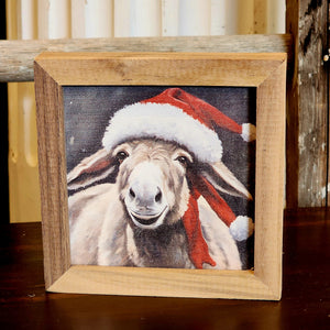 This donkey is too cute to pass up!  Ready for the holidays with his Santa hat, he's ready to come join you for some holiday cheer this year!  It is made from high-quality American hardwood planks with a hand-painted face, printed with UV-cured ink, and framed in a natural walnut frame. Each piece is unique with its own personality, marks, wood grain, and look. Easy to clean with a dry cloth.  Made in the USA  4" x 4" x 1"