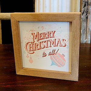 This cool retro "Merry Christmas To All" sign is in pretty pink & turquoise and has scrolls all around the words and a vintage ornament down below.  It is made from high-quality American hardwood planks with a hand-painted face, printed with UV-cured ink, and framed in a natural walnut frame. Each piece is unique with its own personality, marks, wood grain, and look. Easy to clean with a dry cloth.  Made in the USA  4" x 4" x 1"