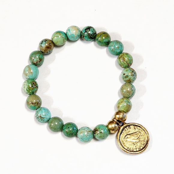 Wear one or stack them high. Our Gemstone Stretch Beaded Bracelets go with anything. Beautiful blue turquoise is threaded on a stretch band and has two gold beads with a gold coin on it.  On one side of the coin is a bird with the date 1938 above and the word 
