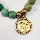 Wear one or stack them high. Our Gemstone Stretch Beaded Bracelets go with anything. Beautiful blue turquoise is threaded on a stretch band and has two gold beads with a gold coin on it.  On one side of the coin is a bird with the date 1938 above and the word "FARTHING" below. On the back side is a man's side profile with letters all around the coin.