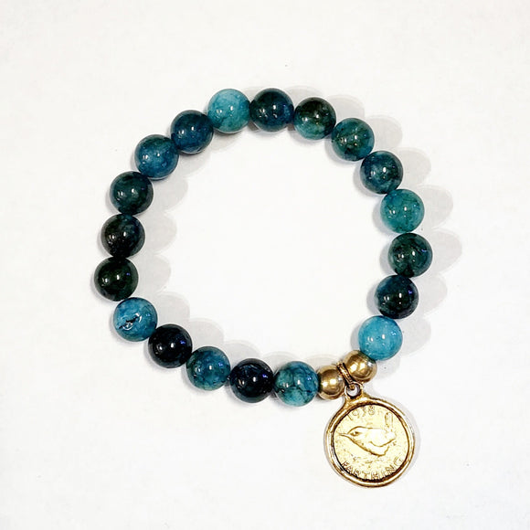 Wear one or stack them high. Our Gemstone Stretch Beaded Bracelets go with anything. Beautiful blue apatite beads are threaded on a stretch band with two gold beads and a gold coin on it.  On one side of the coin is a bird with the date 1938 above and the word 