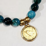 Wear one or stack them high. Our Gemstone Stretch Beaded Bracelets go with anything. Beautiful blue apatite beads are threaded on a stretch band with two gold beads and a gold coin on it.  On one side of the coin is a bird with the date 1938 above and the word "FARTHING" below. On the back side is a man's side profile with letters all around the coin.