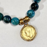 Wear one or stack them high. Our Gemstone Stretch Beaded Bracelets go with anything. Beautiful blue apatite beads are threaded on a stretch band with two gold beads and a gold coin on it.  On one side of the coin is a bird with the date 1938 above and the word "FARTHING" below. On the back side is a man's side profile with letters all around the coin.