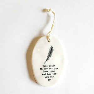 <p><span data-mce-fragment="1">This oval-shaped porcelain ornament is perfect to give to someone to let them know you are thinking of them! Up top is a feather, and below are the words "Take pride in how far you have come and how far you can go."</span></p> <p><span data-mce-fragment="1">2 1/4" W x 3 1/4" H</span></p>