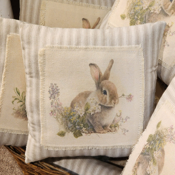 <p>This beautiful neutral pillow will fit in with any spring decor! A sweet little brown bunny is sitting among pretty flowers. The image is printed on cream fabric that has been fringed and then attached to a taupe ticking stripe fabric pillow.<br></p> <p>Approximately 8<span data-mce-fragment=
