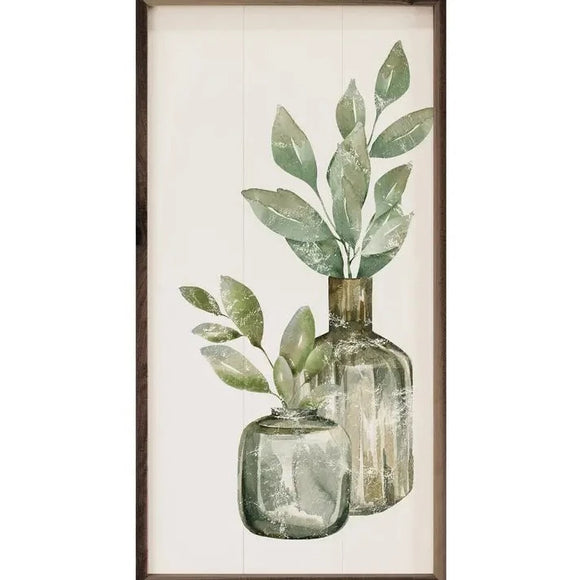 Two different-sized grey-green glass vases have green leaves sticking out of them. On a crisp white pallet background, this picture will ease into any decor!  This unique piece is a simple way to bring beauty and charm to any wall or shelf within the home. It is made from high-quality American hardwood planks with a hand-painted face, printed with UV-cured ink, and is framed in a natural walnut frame.