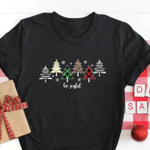 Get in the holiday spirit with this adorable t-shirt! It is soft &amp; super comfortable; you'll never want to take it off! Six different Christmas trees are across the front, with snowflakes between them. The words "Be Joyful" are in a cursive white font.