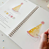 An invitation to slow down and paint something pretty. The Celebrate Watercolor Workbook features twelve party illustrations — balloons, a wrapped gift, a confetti birthday cake, a pup in a party hat, and more — each outlined and ready to paint. Simple step-by-step instructions walk you through every illustration, and most paintings take about thirty minutes from start to finish — so even if you've never painted before, you'll have something lovely in your hands by the end. A sweet birthday gift, or an easy