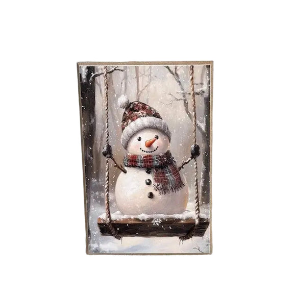 Add a joyful swirl of winter whimsy to your home with this Swinging Snowman! This jolly snowman is bundled in a plaid scarf and floral pom-pom hat, gleefully swaying on a rustic wooden swing. Snow gently falls through a quiet forest backdrop, capturing the magic and innocence of wintertime fun. On a solid wood block, this freestanding piece is ideal for seasonal decorating. Whether placed on a tiered tray, shelf, desk, or windowsill, it brings a cozy, cheerful spirit to any space.

4