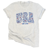 This graphic tee is a perfect blend of style and comfort! We love the retro university-style block blue print with blue and red foral on the inside of the letters USA on a light grey t-shirt. Be;pw are stars on either side of "EST. 1776"&nbsp; What a great summer tee this will be! Crafted with premium materials, it offers a super soft feel.&nbsp;