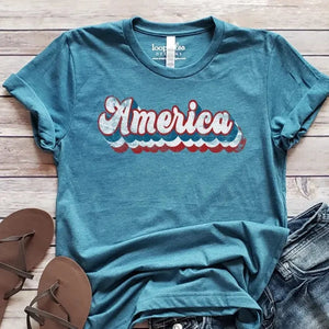 <p>We love this heathered teal tee with "America" in a groovy "Recoleta" 70's white font, outlined in red, white, and blue.</p> <p><span style="font-size: 0.875rem;">This t-shirt is direct-to-fabric printing for a soft design that won't crack or peel. The shirts are soft Bella and Canvas unisex fashion-fit tees that fit like a well-loved favorite, featuring a crew neck and short sleeves.</span></p>