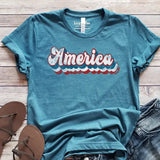 <p>We love this heathered teal tee with "America" in a groovy "Recoleta" 70's white font, outlined in red, white, and blue.</p> <p><span style="font-size: 0.875rem;">This t-shirt is direct-to-fabric printing for a soft design that won't crack or peel. The shirts are soft Bella and Canvas unisex fashion-fit tees that fit like a well-loved favorite, featuring a crew neck and short sleeves.</span></p>