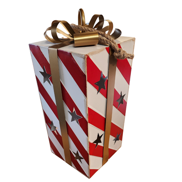 You'll love adding this festive red and white distressed striped package with a gold ribbon in it. There are star cutouts along all sides that let light from a LED votive or battery powered candle show through (there is no base, so it is easy to just sit on top of your light source). At the top is a gold ring at the center of the bow in case you would like to hang.

Approximatly 9.75