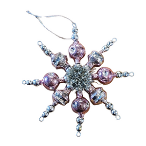 This retro-inspired ornament features pink hand-crafted glass beads threaded together to form a star and&nbsp;a tinsel center for some yesteryear charm!

1" H x 6 1/2" Dia

Glass&nbsp;