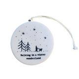 "Walking in a winter wonderland" Porcelain Heart Ornament has two pine trees on the left with a person walking their dog to the right as snow is falling all around. On the back are three pine trees under the stars and moon with snow all around.  2 1/2" Dia