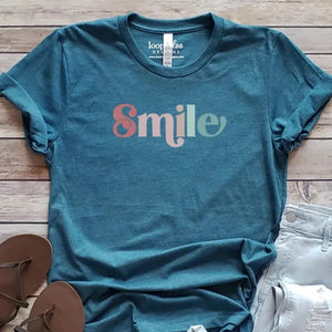 This fun retro-styled "Smile" tee has fun multi-colored letters printed on heathered teal fabric. It has direct-to-fabric printing for a soft design that won't crack or peel. The shirts are soft Bella and Canvas unisex fashion-fit tees that fit like a well-loved favorite, featuring a crew neck and short sleeves.  100% Airlume combed and ring-spun cotton.  Made in the United States