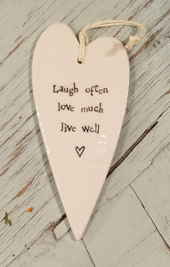 a porcelain white heart shaped ornament with a white cord to hang with the words "Laugh often love much live well"
