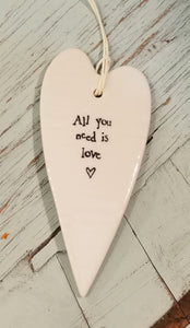a porcelain white heart shaped ornament with a white cord to hang with the words "all you need is love"