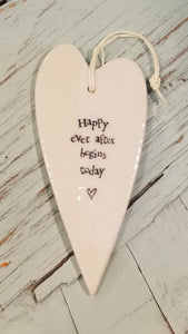 a porcelain white heart shaped ornament with a white cord to hang with the words "happy ever after begins today"