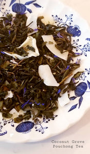 Coconut Grove Puchong Tea: A loose-leaf pouchong tea with blue cornflower petals in it and shaved slices of coconut all on a blue and white patterned plate.