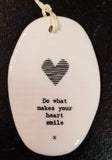 A white oval porcelain ornament with ridges going horizontally.  On the ornament is a line drawing of a heart and underneath is "Do what makes your heart smile" *  in a black typeset font