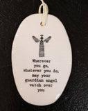 A white oval porcelain ornament with ridges going horizontally.  On the ornament is a line drawing of an angel and underneath is "Wherever you go, whatever you do, may your guardian angel watch over you" *  in a black typeset font