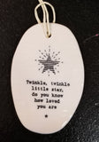 A white oval porcelain ornament with ridges going horizontally.  On the ornament is a line drawing of a star and underneath is "Twinkle, twinkle little star, do you know how loved you are" *  in a black typeset font