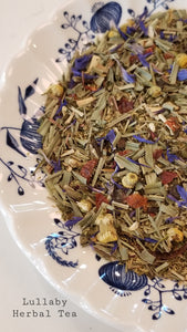 Lullaby tea: herbs & fruit: lemongrass, peppermint, camomile, rosehip, spearmint, valerian root, hibiscus, cornflower petals, natural flavors that are organic compliant. The loose herbs and fruit are on a white plate with a blue onion pattern design.