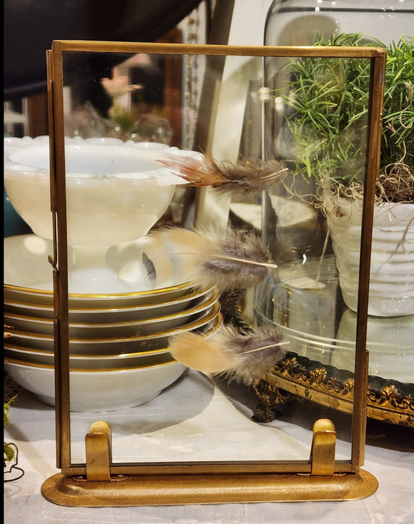 This brass frame has a hinged door to open and put a picture in.  We've added feathers for fun, but think out of the box...concert tickets, postcards, or cherished recipes would work too! The frame then slides into a brass base to sit upright.  Frame is 5.25