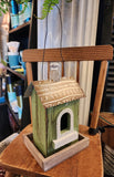 This wooden birdhouse has a pretty green finish with a cute window with white trim on the front.  The base is wood, and the roof is a distressed brown metal with a wooden finial on top.  There is a black wire on top for easy hanging.  5.5"W x 4.75"D x 8.5"H