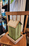 This wooden birdhouse has a pretty green finish with a cute window with white trim on the front.  The base is wood, and the roof is a distressed brown metal with a wooden finial on top.  There is a black wire on top for easy hanging.  5.5"W x 4.75"D x 8.5"H