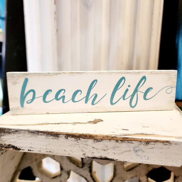 This mini sign has a white washed background with turquoise marks, and the words 