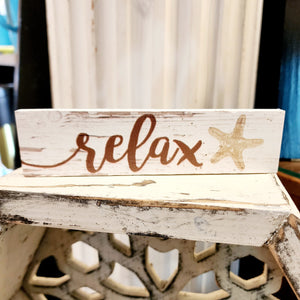 Ahhhh.... R-E-L-A-X!!! This mini sign has a whitewashed wooden background with the word "relax" in a brown cursive font.  On the right is a tan starfish.  Wood. Depth: 0.4375" Width: 6" Height: 1.5"