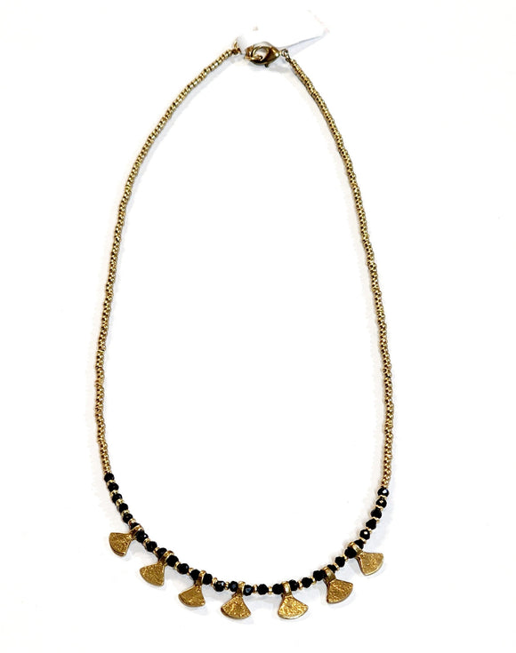 This gold beaded necklace with glass black beads and has 7 gold triangle shapes hanging from the bottom. It is pretty to wear alone but looks great layered with one of our longer brass necklaces!  Handmade by a young designer and team of artists in Northern India.  17