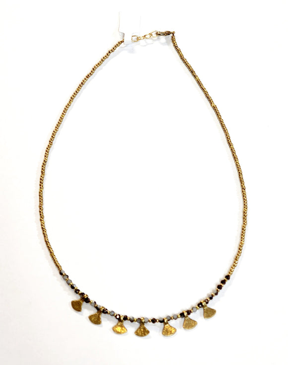 This gold beaded necklace with gray multicolored glass beads has 7 gold triangle shapes hanging from the bottom. It is pretty to wear alone but looks great layered with one of our longer brass necklaces!  Handmade by a young designer and team of artists in Northern India.  17