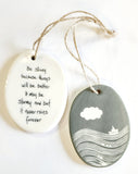 We love our porcelain ornaments because they are perfect for gift-giving! This oval ornament says, "Be strong because things will be better.  It may be stormy now, but it never rains forever" on one side. On the other side is a grey background with a cloud over the water with a sailboat in white.   Dimensions: 2" W x 2 3/4" H