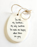 We love our porcelain ornaments because they are perfect for gift-giving! This oval ornament says, "You are my sunshine, my only sunshine.  You make me happy when skies are grey" on one side. On the other side is a grey background with a white dandelion puff.   Dimensions: 2" W x 2 3/4" H