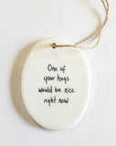 We love our porcelain ornaments because they are perfect for gift-giving! This oval ornament says, "One of your hugs would be nice right now" on one side. The other side has a grey background with a single branch with leaves in white.  Dimensions: 2" W x 2 3/4" H