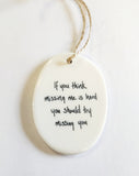 We love our porcelain ornaments because they are perfect for gift-giving! This oval ornament says, "If you think missing me is hard you should try missing you" on one side. The other side has a grey background with a branch running the center with leaves and berries on either side.  Dimensions: 2" W x 2 3/4" H