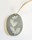 We love our porcelain ornaments because they are perfect for gift-giving! This oval ornament says, "If you think missing me is hard you should try missing you" on one side. The other side has a grey background with a branch running the center with leaves and berries on either side.  Dimensions: 2" W x 2 3/4" H