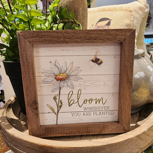 We love this sweet little sign! It has a daisy on the left with a bee buzzing around on the right above the words "Bloom where you are planted" in a mixed font.  It is made from high-quality American hardwood planks with a hand-painted face, printed with UV-cured ink, and framed in a natural walnut frame. Each piece is unique with its own personality, marks, wood grain, and look. Easy to clean with a dry cloth.  Made in the USA  4" x 4" x 1"