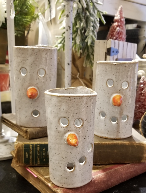 three white snowmen votives with a speckled pattern in the glaze sitting on books. Left snowman has two eyes, a carrot nose and an 