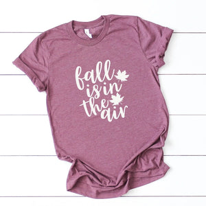 Celebrate FALL with a t-shirt in the prettiest shade of heathered plum.  It says "Fall is the Air" with a leaf along the side in white. These are so soft & comfy, you will love wearing them to ball games, bonfires or just running around doing errands. The styling possibilities are endless. Roll up the sleeves, tie a side knot, front tuck, or wear it while lounging around the house. We guarantee that you will love this shirt's fit and softness.  