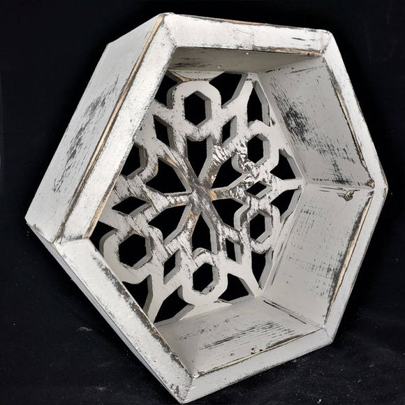 A white distressed wood hexagon shelf with a pierced back that looks similar to a snowflake design. It has 3.5